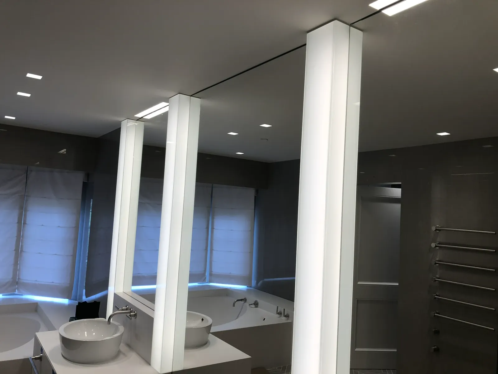Vanity wall of mirrors divided by vertical frosted-glass light pillars