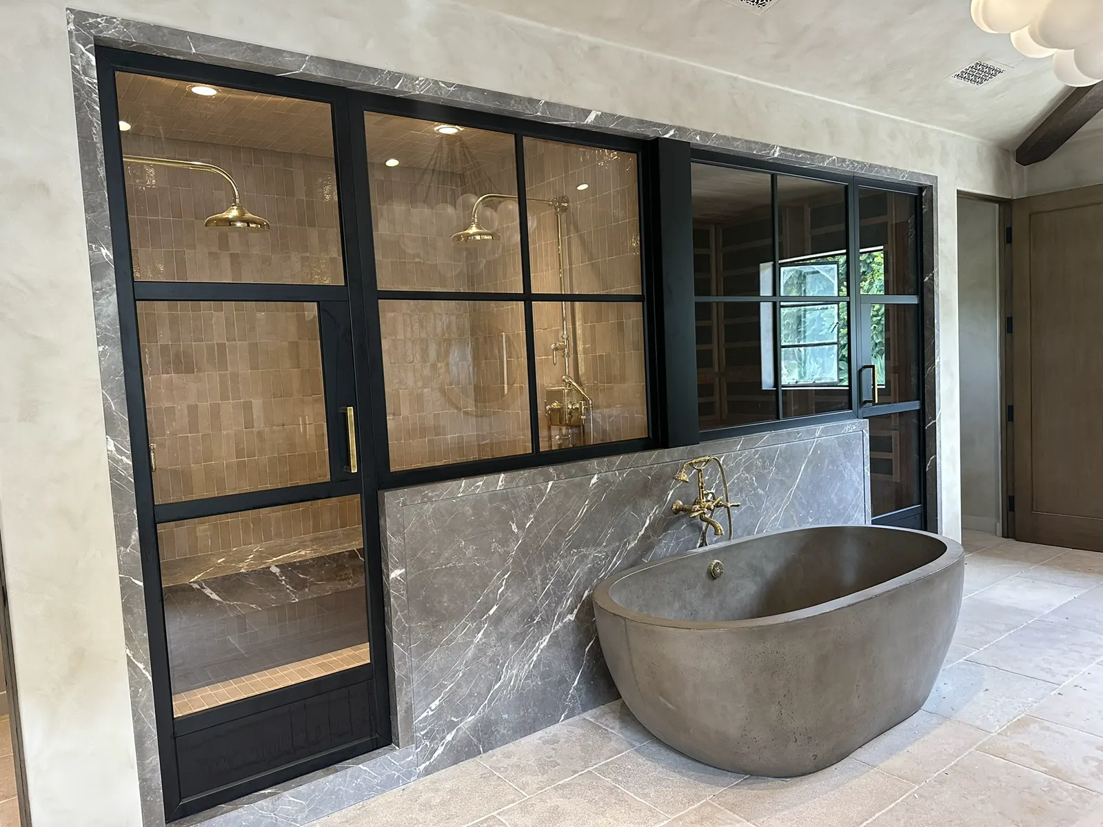 Black metal-framed glass partition separating a shower and stone tub