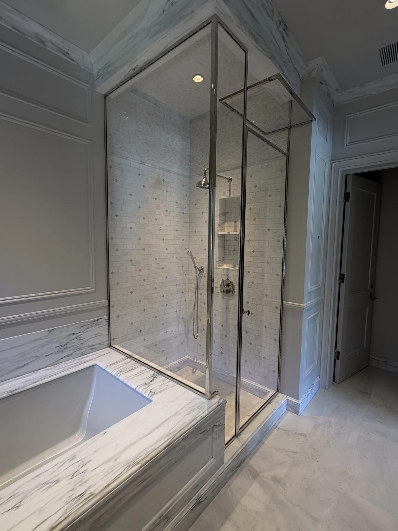 Chrome-framed glass shower next to a marble tub